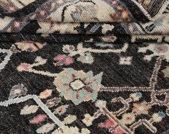 Puede incluir: Una alfombra negra con un patrón floral en tonos de rosa, azul y blanco. La alfombra tiene un aspecto desgastado y está hecha de un material suave y tejido.