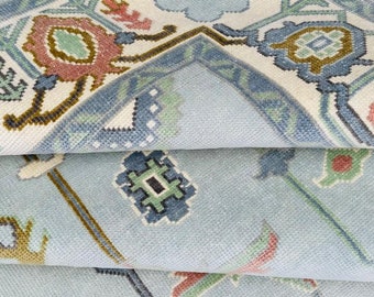 May include: A light blue rug with a geometric pattern in shades of green, brown, and pink. The rug has a fringed edge.