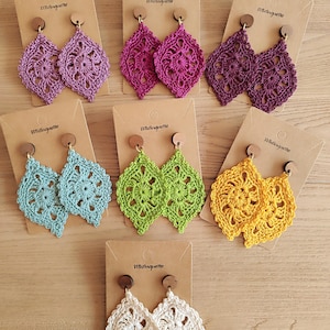 Peut inclure: Six paires de boucles d'oreilles en crochet présentées sur des cartes. Les boucles d'oreilles sont de différentes couleurs, notamment le violet, le rose, le vert, le bleu, le jaune et le blanc. Chaque paire est fixée à un poteau en bois.