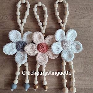 May include: Three crocheted flower wall hangings with wooden bead strands. The flowers are in shades of white, pink, and grey. The beads are natural wood colour. The text "Crochetmistinguette" is visible at the bottom of the image.