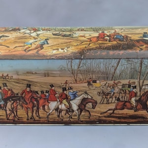 Puede incluir: Caja metálica rectangular con tapa, que presenta una detallada escena de caza con jinetes a caballo, perros y un paisaje. La caja tiene un diseño vintage con una ilustración colorida.