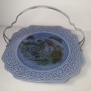 Może przedstawiać: Błękitna ceramiczna taca do serwowania z srebrnym uchwytem. Taca przedstawia scenę polowania z jeźdźcem na koniu i psami. Na tacy nadrukowany jest tekst "The Chase".