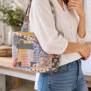 May include: A rectangular tote bag featuring a patchwork design with various fabric patterns including blue and white gingham, yellow stripes, and floral prints in shades of pink, blue, and green, complete with two matching fabric shoulder straps.