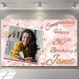 Puede incluir: Una pancarta rosa y dorada con una foto de una persona sonriente. La pancarta dice "Congrats!! Happy 30th Birthday Janet" en escritura dorada. Diseños florales y geométricos decoran la pancarta, creando un tema de celebración.