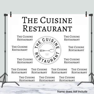 May include: A white backdrop with the text "THE CUISINE RESTAURANT" in black. A black and white logo with the text "THE CUISINE RESTAURANT" and a spoon graphic is centered on the backdrop. The text "THE CUISINE RESTAURANT" is repeated multiple times in black on the backdrop.