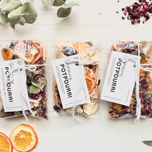 May include: Three small bags of dried potpourri tied with twine. Each bag has a white tag with the text "Smelling Potpourri" written in black cursive. The bags contain dried orange slices, lavender, and other botanicals.