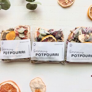 May include: Three clear plastic bags filled with dried fruit, herbs, and flowers. Each bag has a white label that reads "Simmering Potpourri" with the text "Organic & Vegan" in the corner.