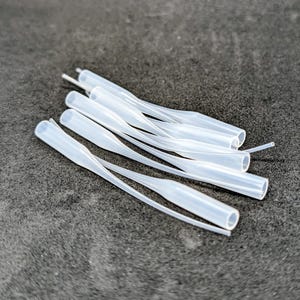 Könnte beinhalten: Ein Set aus drei Keramikbechern mit einer gesprenkelten, cremefarbenen Glasur. Jeder Becher hat ein anderes handgemaltes Design: ein blaues und grünes Blatt, eine gelbe und orangefarbene Blume und ein roter Beerenzweig. Die Becher haben eine einfache, abgerundete Form.