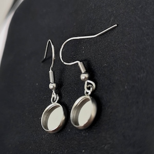 Könnte beinhalten: Ein Paar silberne Ohrhänger mit runden, offenen Fassungen. Die Ohrringe sind aus Metall und haben ein schlichtes, minimalistisches Design.