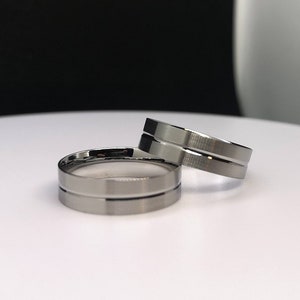 May include: Two silver wedding bands with a grooved design. The bands are on a white surface.