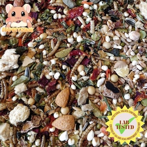 May include: A close-up of a mix of dried foods for small pets, including seeds, dried fruits, and insects. The mix is labelled "Nutritional Values Confirmed Lab Tested Certified by ISO and UKAS Independent Laboratory".