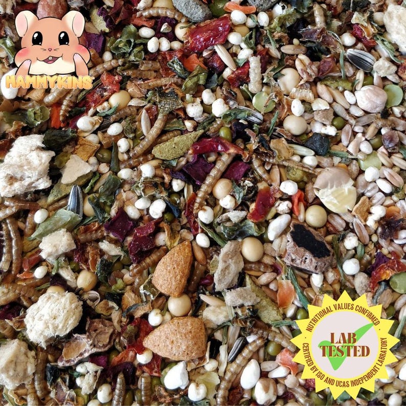 May include: A close-up of a mix of dried foods for small pets, including seeds, dried fruits, and insects. The mix is labeled "Nutritional Values Confirmed Lab Tested Certified by ISO and UKAS Independent Laboratory".