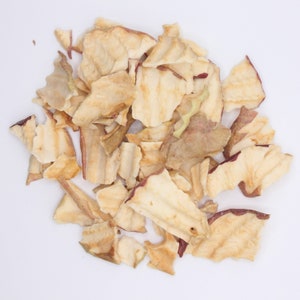 May include: A pile of dried apple slices, some with a reddish hue, on a white background.