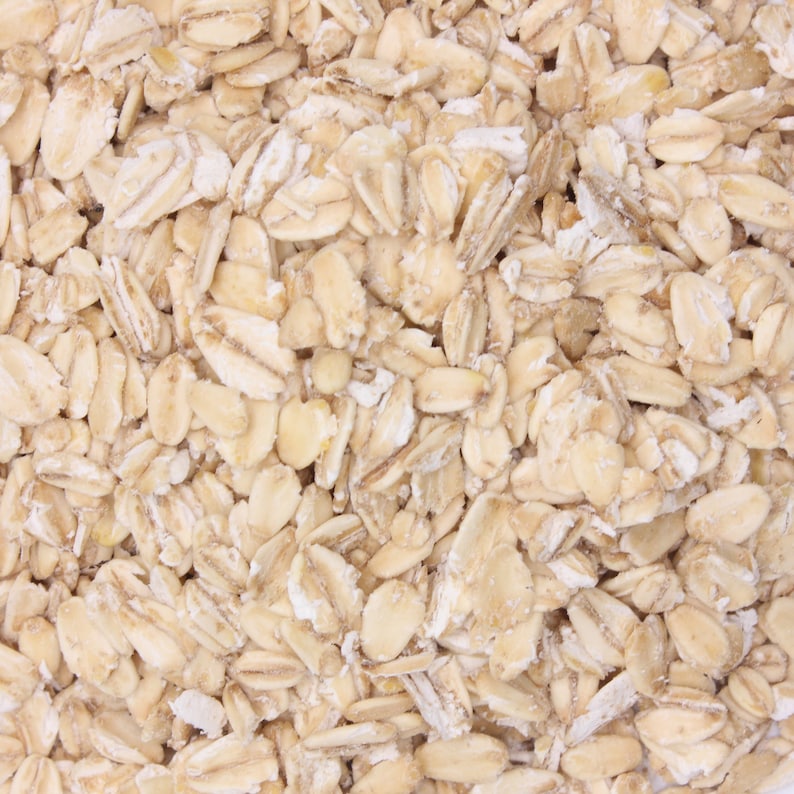 May include: Close-up of a pile of uncooked rolled oats. The oats are a light beige color and have a slightly grainy texture.