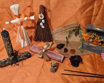 May include: A collection of witchy items including a corn husk doll, a broom, a scroll, a small wooden box with dried flowers, a black candle, a black incense stick, a small black figurine, and a few crystals.