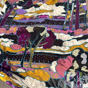 May include: A colorful fabric with a landscape design. The pattern features trees, clouds, and abstract shapes in shades of purple, pink, yellow, and black. The fabric has a textured appearance.