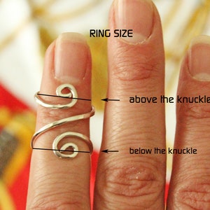 May include: A silver ring with a spiral design is shown on a finger. The ring is measured above and below the knuckle to determine the correct size.  RING SIZE is written above the finger.