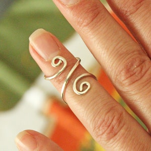 May include: A silver ring with a swirling design, worn on a finger.