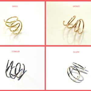 Op de afbeelding: Vier close-up afbeeldingen van een drievoudige spiraal oormanchet in verschillende metaalafwerkingen: messing, brons, titanium en zilver.