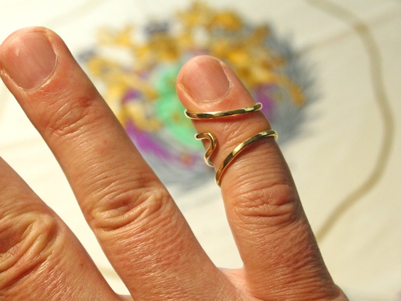Op de afbeelding: Een gouden ring met een gedraaid ontwerp, gedragen aan een vinger.