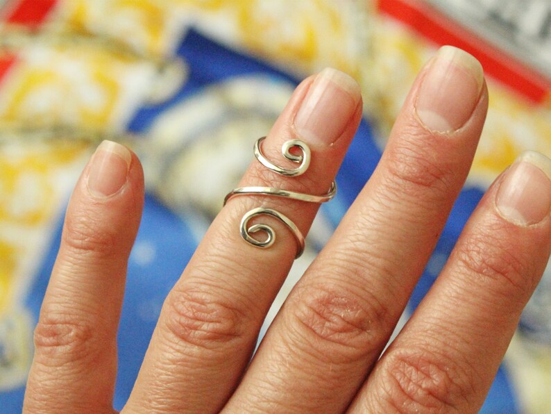 May include: A silver ring with a unique, swirling design. The ring is worn on the middle finger of a hand.
