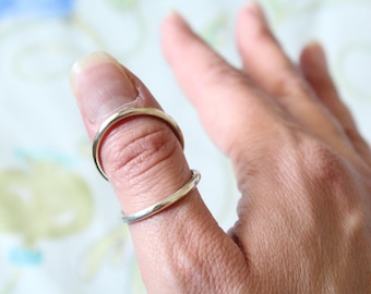 Può includere: Due anelli d'argento indossati sul pollice di una persona.