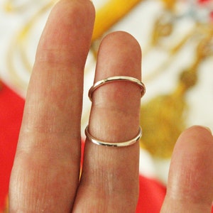 May include: Two silver rings stacked on a finger. The rings are simple and plain.