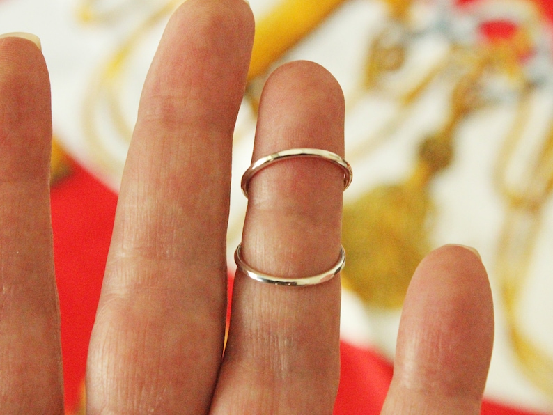 May include: Two silver rings stacked on a finger. The rings are simple and plain.