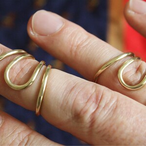 K&ouml;nnte beinhalten: Zwei goldfarbene Ringe, einer an jedem Finger, sind spiralf&ouml;rmig um die Finger gewickelt. Die Ringe sind aus dickem, glattem Metall.