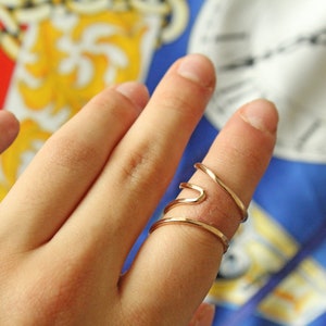 Op de afbeelding: Een gouden, dubbel gewikkelde ring met een uniek, golvend ontwerp. De ring wordt gedragen aan de wijsvinger van een hand.