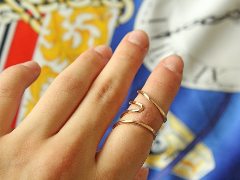 Op de afbeelding: Een gouden, dubbel gewikkelde ring met een uniek, golvend ontwerp. De ring wordt gedragen aan de wijsvinger van een hand.