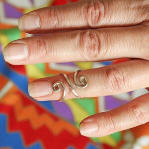 May include: A silver ring with a swirling design, worn on a finger.