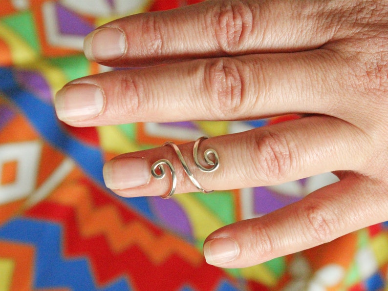 May include: A silver ring with a swirling design, worn on a finger.