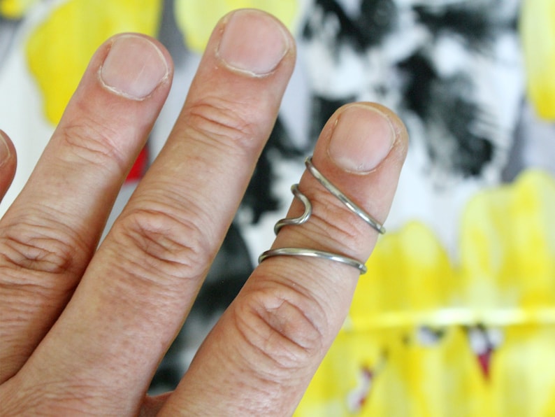 Op de afbeelding: Een zilveren ring met een uniek, gedraaid ontwerp. De ring wordt gedragen aan de middelvinger van een hand.