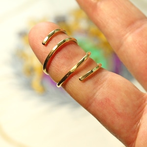 Op de afbeelding: Drie gouden ringen gestapeld op een vinger. De ringen zijn simpel en hebben een gehamerde textuur.