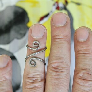 May include: A silver ring with a unique, twisted design. The ring is worn on the middle finger of a hand.