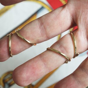 K&ouml;nnte beinhalten: Zwei goldfarbene Ringe, einer an jedem Finger, sind zweimal um die Finger gewickelt. Die Ringe sind schlicht und haben eine glatte, polierte Oberfl&auml;che.