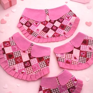 May include: Pink bibs with a patchwork design featuring hearts, cherries, and the word "Love". Each bib has a pink collar and a ruffled edge. The bibs are arranged on a pink surface with heart-shaped decorations.
