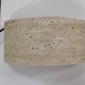 May include: A light beige, round, stone lampshade with a textured surface.