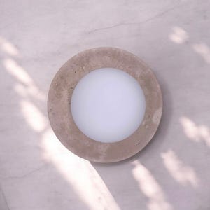 Puede incluir: Un macetero redondo de hormigón con un interior blanco liso. El macetero tiene un exterior rugoso y texturizado.