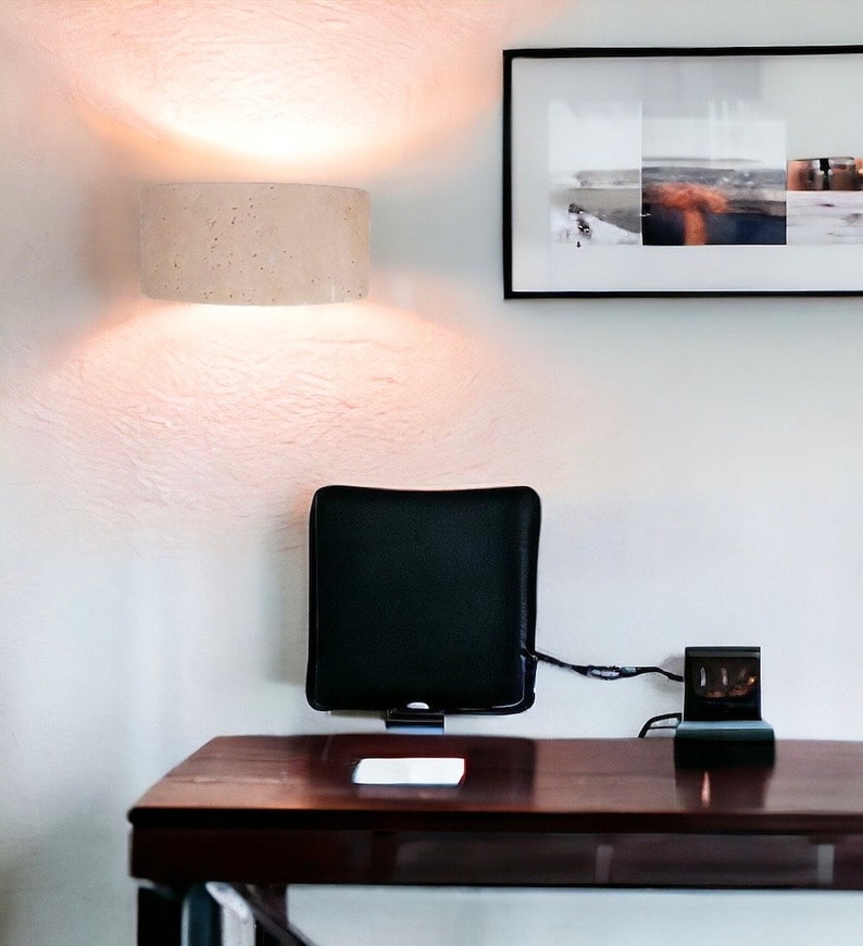 May include: A dark brown wooden desk with a black cushion attached to the wall, a black electrical outlet with a cord running to the cushion, and a white rectangular object on the desk. A white ceiling light fixture is mounted on the wall above the desk.