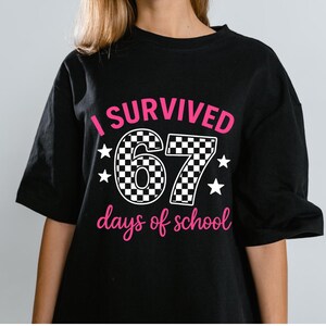 Puede incluir: Camiseta negra con el texto rosa "I SURVIVED 67 days of school". El número 67 tiene un diseño de cuadros y estrellas blancas. Un diseño divertido para el fin de curso.