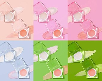 May include: A selection of lip balms in clear, square containers with heart-shaped lids. The balms are presented against pink, green, and blue backdrops. Each balm has a unique colour and texture, with some appearing shimmery and iridescent.