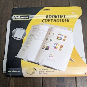 May include: A white plastic book holder with the text "Booklift Copyholder" on the front of the packaging. The packaging is yellow and black with the brand name "Fellowes" on the top left corner. The product is designed to hold textbooks, reference manuals, and daily planners.