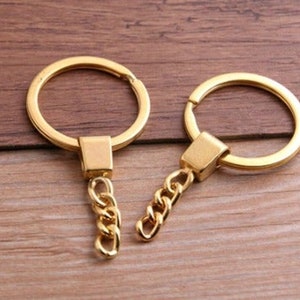May include: Two gold keychains with a circular ring and a chain. The keychains are on a wooden surface.