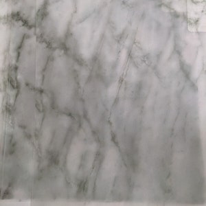 May include: A close-up of a white marble surface with gray veining. The surface is smooth and polished.