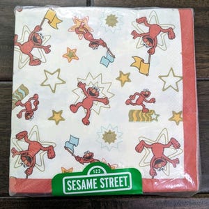 以下が含まれることがあります： セサミストリートのナプキンパック。エルモ、旗、星の繰り返し模様。ナプキンは白い背景、赤い縁取り、セサミストリートのロゴ入り。プラスチック包装。