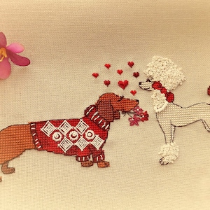 May include: Cross-stitch image of two dogs in love. A brown dachshund wearing a red sweater with a white geometric design offers flowers to a white poodle with a red bow. Red hearts float between them.
