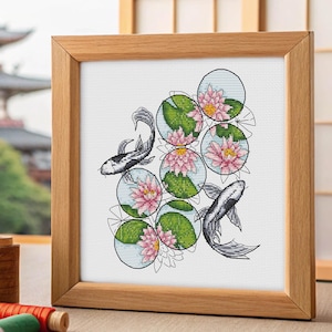 Könnte beinhalten: Gerahmtes Kreuzstich-Kunstwerk mit einer japanischen Koi-Teich-Szene. Das Design zeigt schwarz-weiße Koi-Fische, rosa Seerosen und grüne Seerosenblätter in kreisförmigen Blasen. Der Rahmen besteht aus hellem Holz.