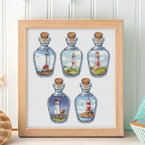 Peut inclure: Une œuvre d'art encadrée présentant cinq motifs de point de croix de phares à l'intérieur de bouteilles en verre avec des bouchons en liège. Chaque bouteille présente une scène de phare différente avec des couleurs et des paysages variés.